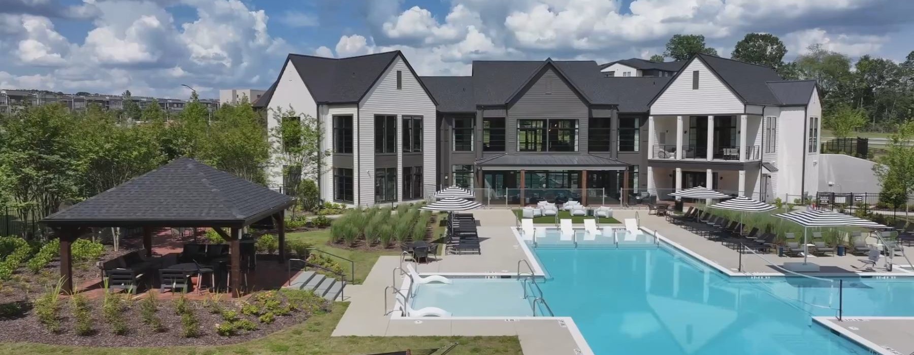 A resort-style pool sits in front of a two-story clubhouse of an apartment complex.